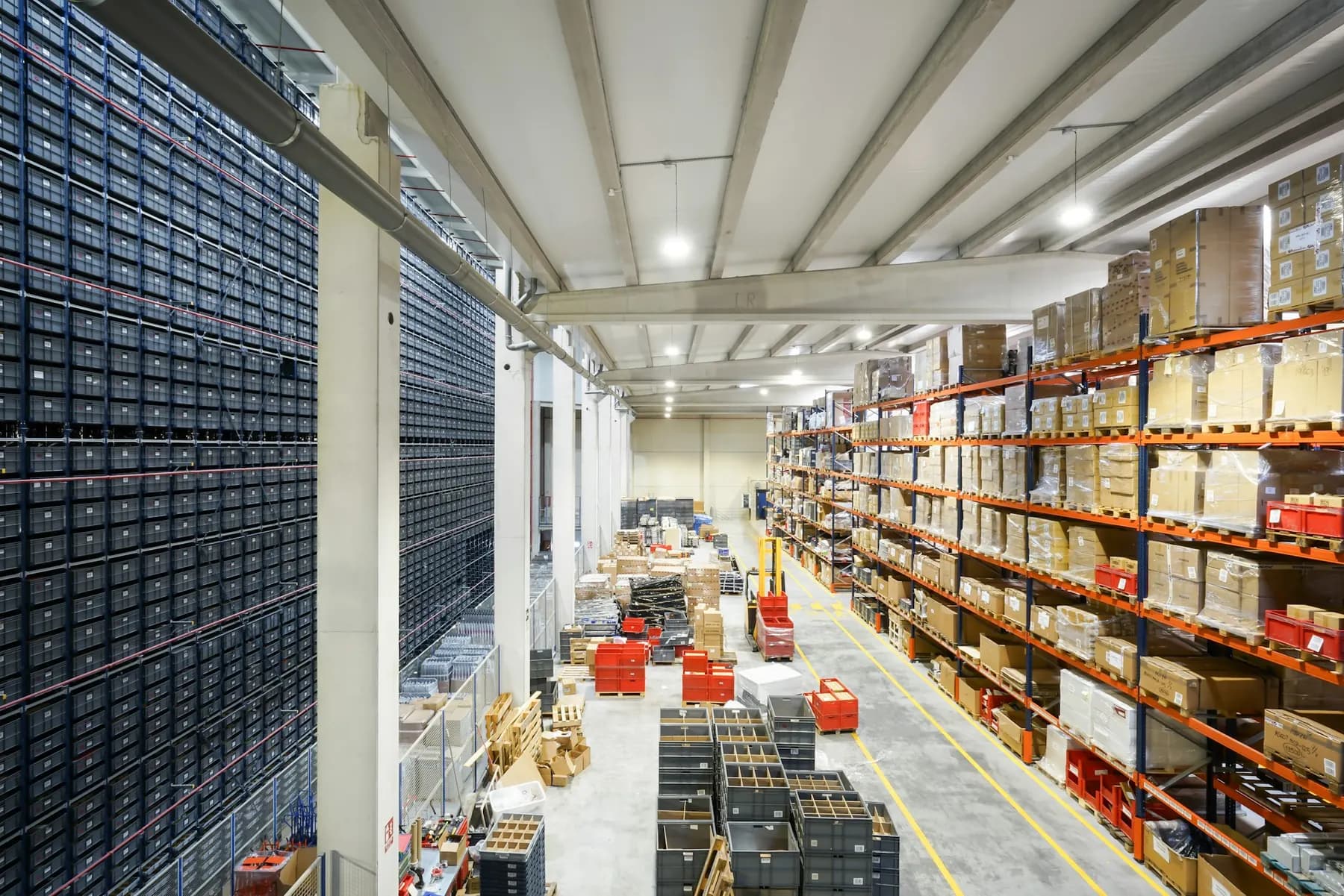 A bright warehouse with racking, boxes and forklifts